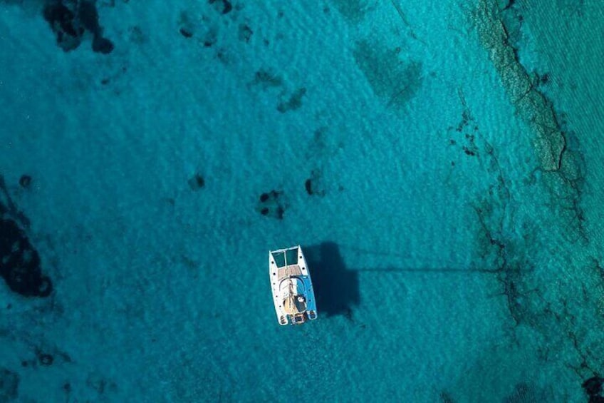 An aerial view of a boat anchored in clear turquoise waters with visible underwater features. 3