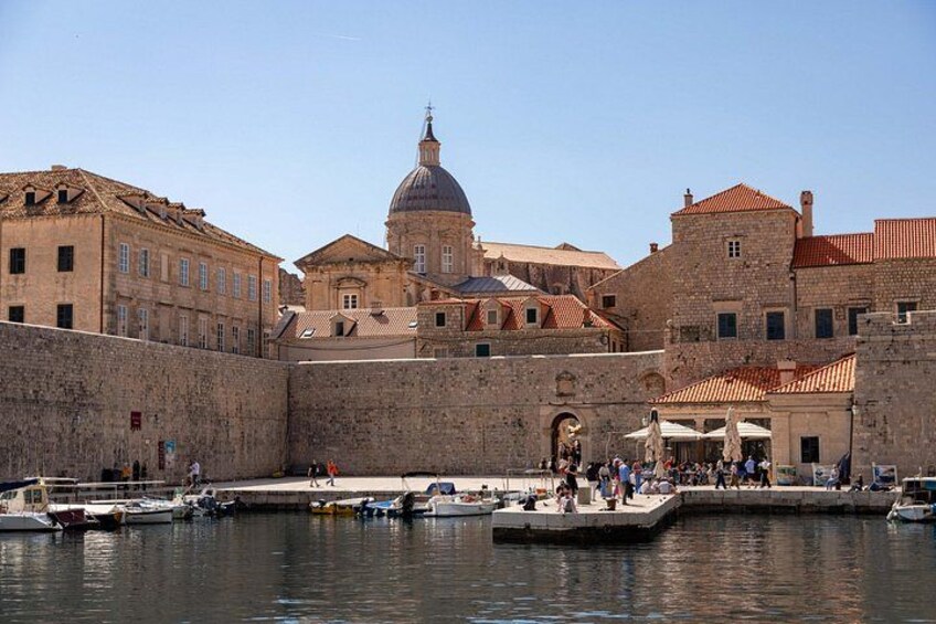 A historic waterfront with stone buildings, a domed structure, and boats docked at the pier. 2