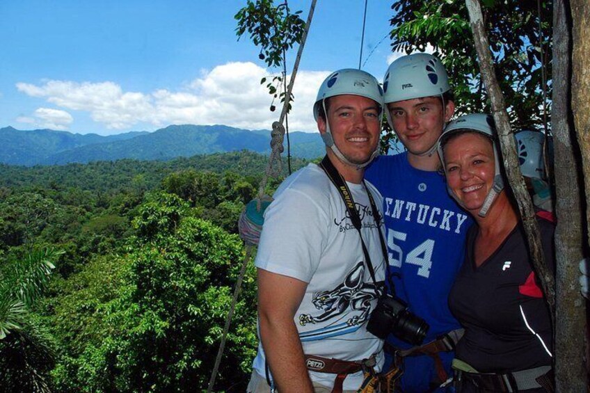 Tres personas con cascos, una con camiseta del Kentucky 54, de pie en una zona boscosa con montañas al fondo. 5