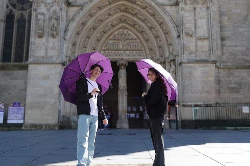 Two people standing in front of a cathedral holding purple umbrellas. 3