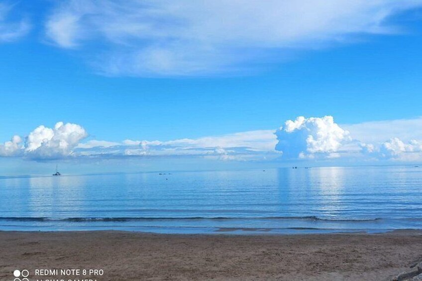 Una playa con agua tranquila, cielo despejado y un velero a lo lejos. 3