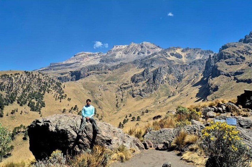 Une personne assise sur un rocher, avec un paysage montagneux en arrière-plan. 2