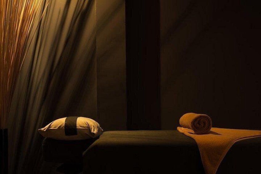 A dimly lit room with a bed, a pillow, and a rolled-up towel. 2