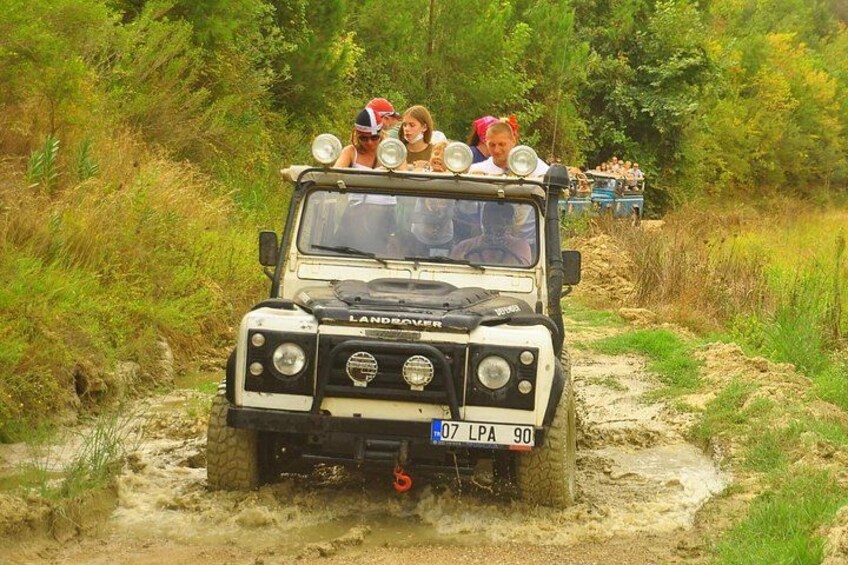 A Land Rover driving through a muddy path with passengers on top. 5