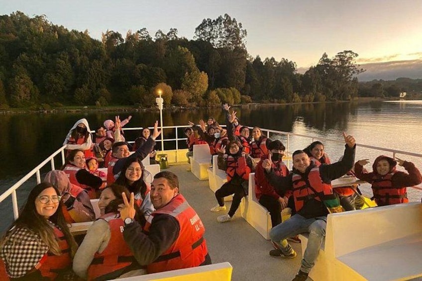 A group of people on a boat, wearing life jackets, with a lake and trees in the background. 2