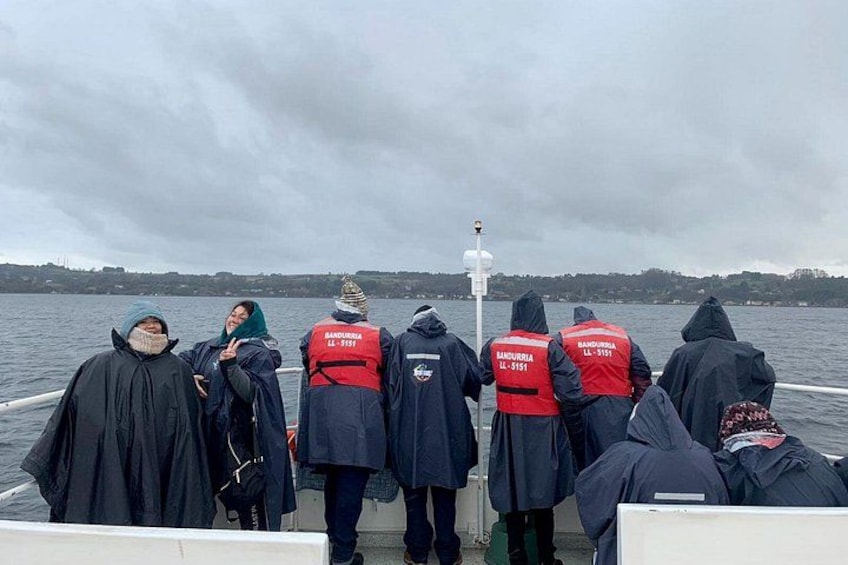Een groep mensen in reddingsvesten op een boot, met een bewolkte lucht en water op de achtergrond. 2
