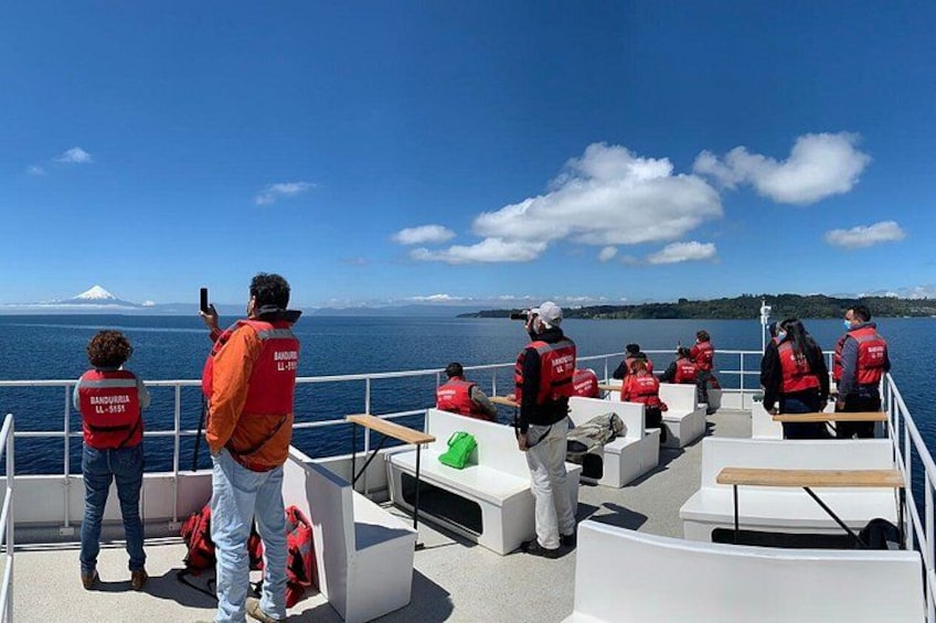 A group of people on a boat wearing red life jackets, with a clear sky and a distant mountain. 1