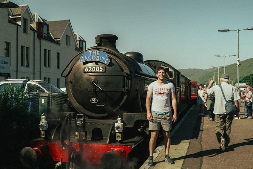 A steam locomotive with the number 62005, a person in a Superman t-shirt, and a crowd of people on a platform. 3