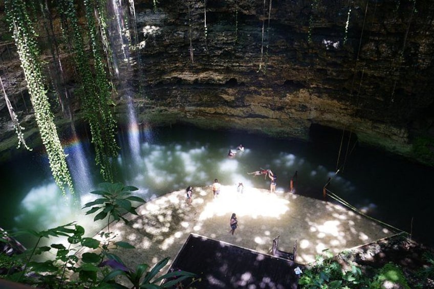 Eine natürliche Felsformation mit einem Wasserfall, einer Plattform mit Personen und umgebender Vegetation. 2