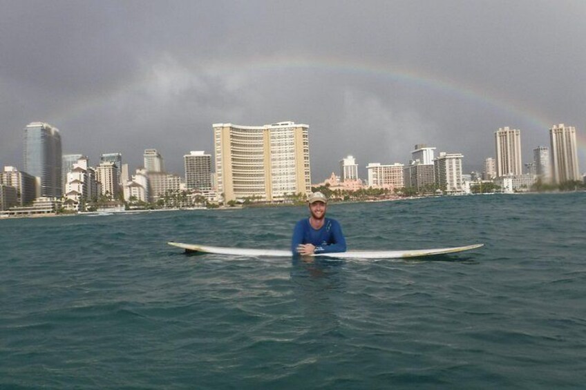 Een persoon op een surfplank in de oceaan, met een stadsachtergrond en een regenboog. 4