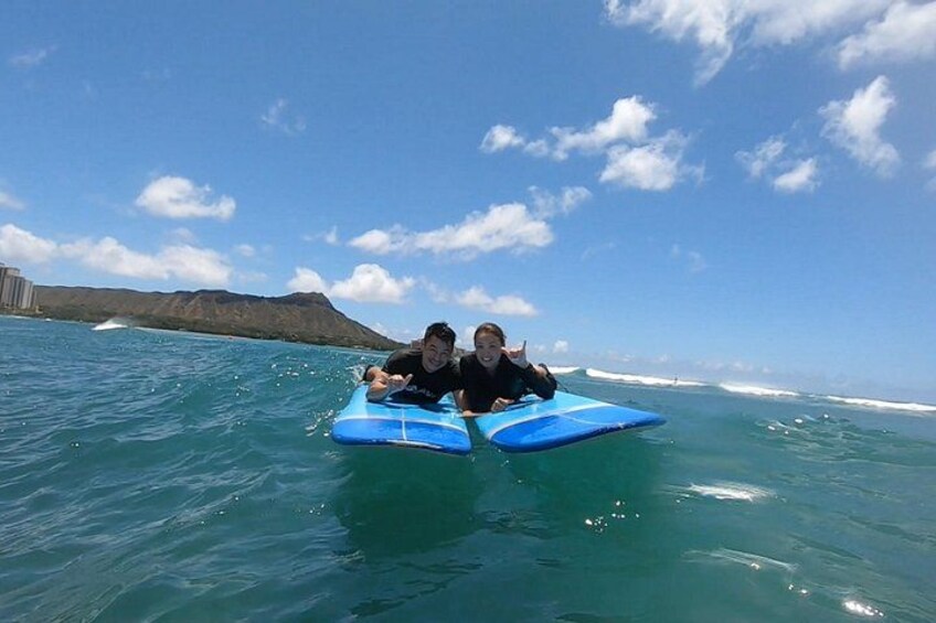 Two people on a blue surfboard in the ocean with a clear sky and distant mountains. 5