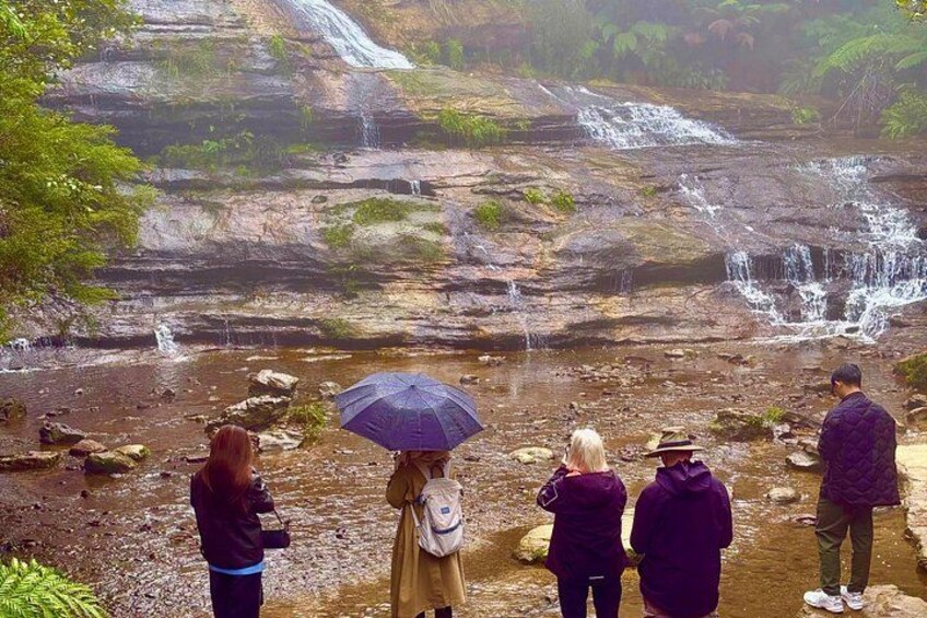 A waterfall cascading over rocks in a forested area with people observing. 4
