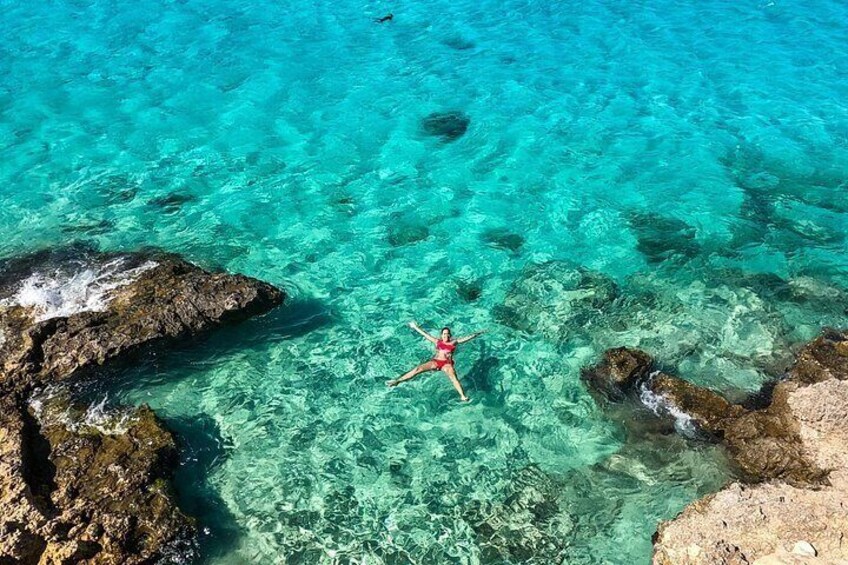 A person swimming in clear turquoise water surrounded by rocky formations. 3