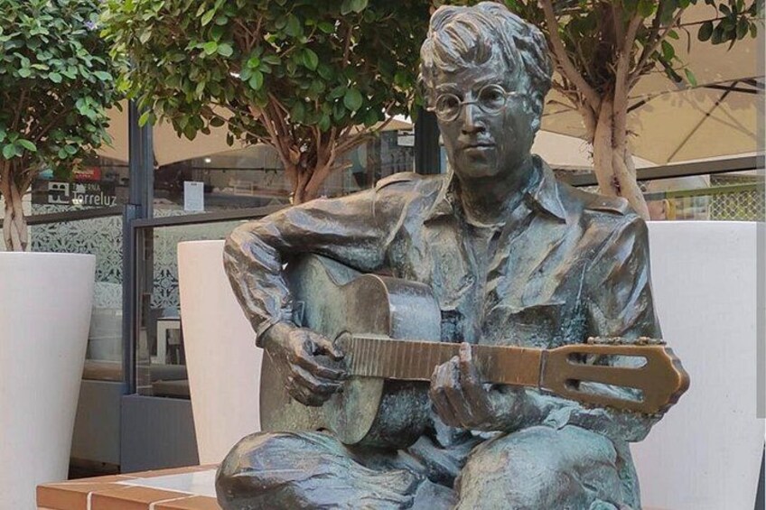 A bronze statue of a seated man playing a guitar. 1