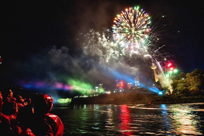 A nighttime fireworks display over a body of water with reflections, a Ferris wheel, and a distant illuminated structure. 4