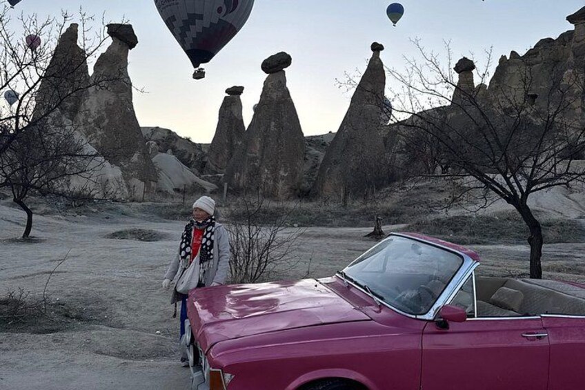 A red convertible car parked in a desert landscape with unique rock formations and hot air balloons in the background. 4