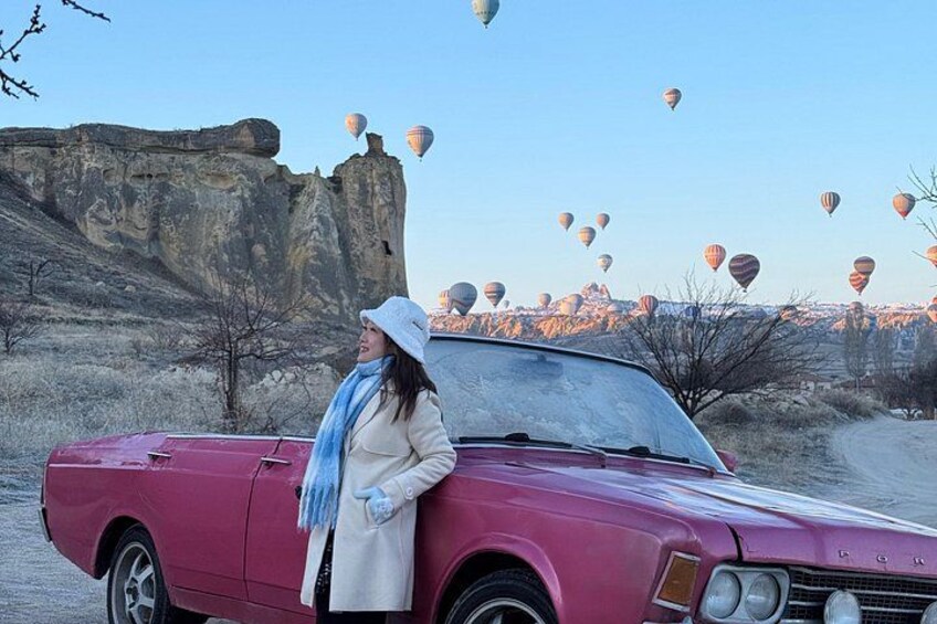 A vintage car parked in a desert landscape with hot air balloons in the background. 3