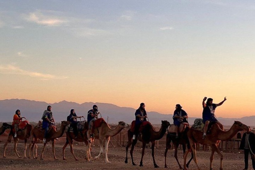 A group of people riding camels on a desert landscape with mountains in the background. 4
