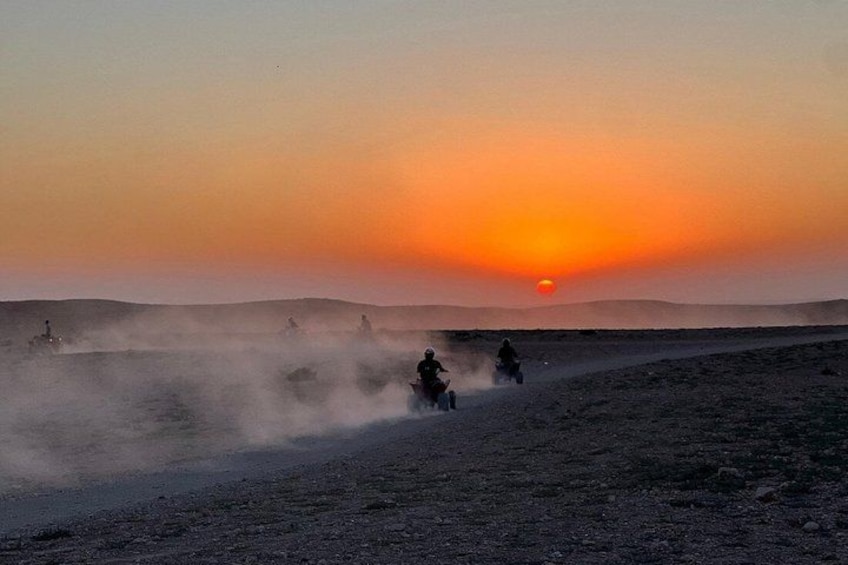 A sunset over a desert landscape with vehicles and riders on a dusty road. 5