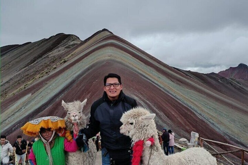 A person standing with two alpacas in front of a colorful mountain range. 4
