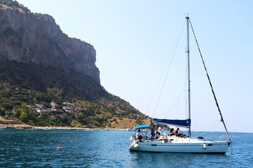 A sailboat on calm waters with a rocky coastline and a cliff in the background. 1