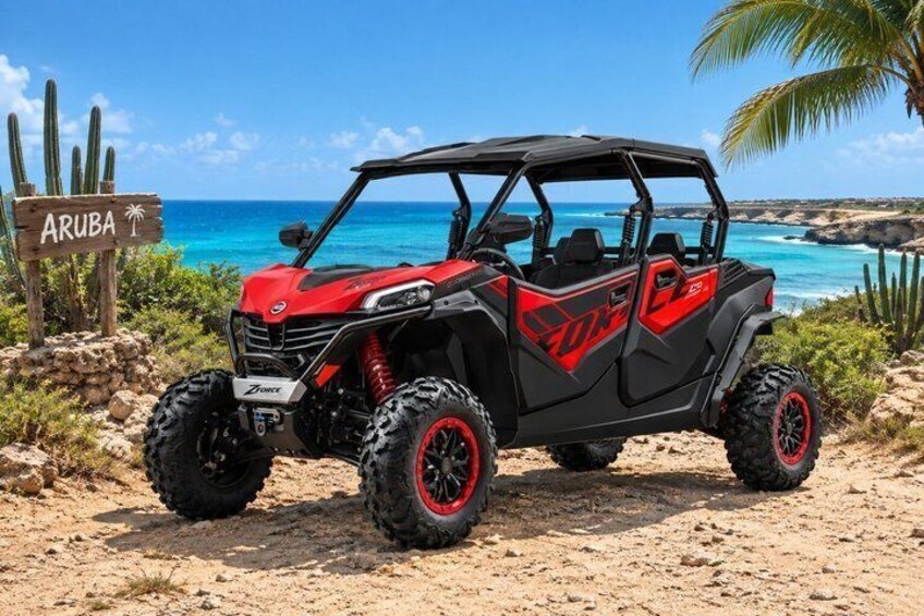A red and black off-road vehicle parked on a sandy beach with a sign reading 'ARUBA' in the background. 2