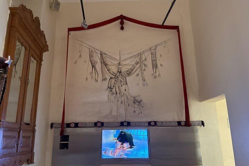 A room with a large tapestry hanging on the wall, a wooden cabinet, and a television screen displaying an animated character. 2