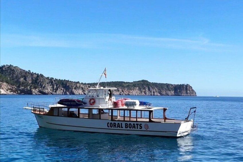 Ein Boot mit dem Namen 'CORAL BOATS' auf ruhigem Wasser, im Hintergrund eine felsige Küste. 4