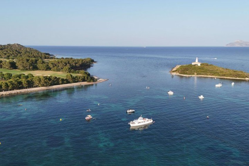 Eine Küstenlandschaft mit einem Leuchtturm auf einer kleinen Insel, klarem, blauem Wasser und mehreren Booten. 3
