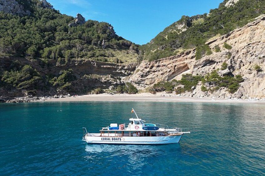 Un bote llamado 'CORAL BOATS' en un mar azul despejado, con acantilados rocosos al fondo. 1