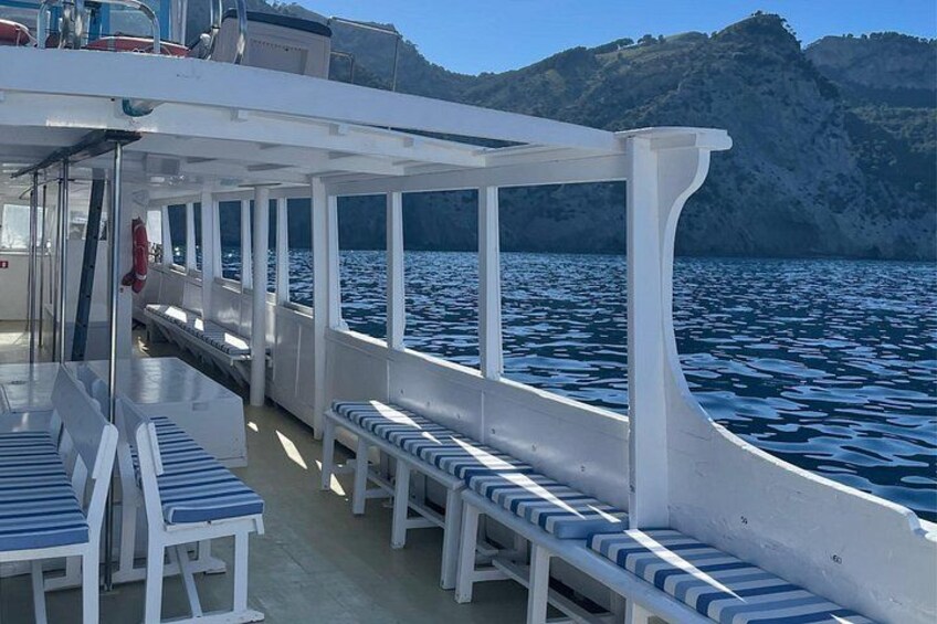 Un bote con barandas blancas y bancos a rayas azules, navegando sobre aguas tranquilas con una costa montañosa al fondo. 4