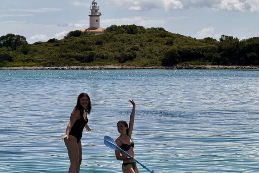 Deux personnes dans l’eau, l’une tenant une planche de surf, avec un phare en arrière-plan. 2