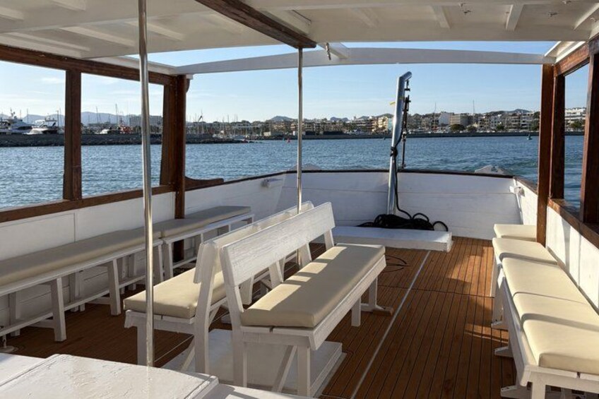 Ein Bootsdeck mit weißen Bänken und Blick auf einen Yachthafen. 5