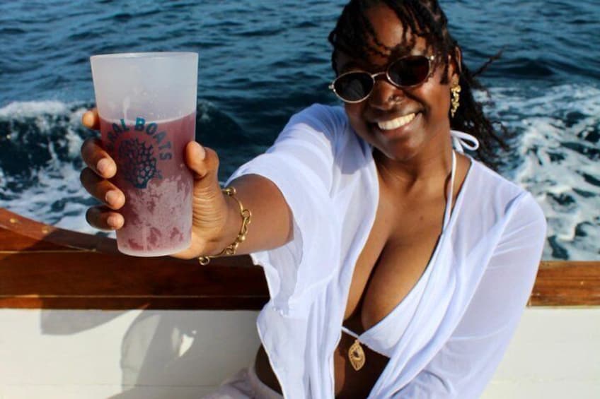 Une personne tenant un verre orné d’un logo, à bord d’un bateau, avec de l’eau en arrière-plan. 5