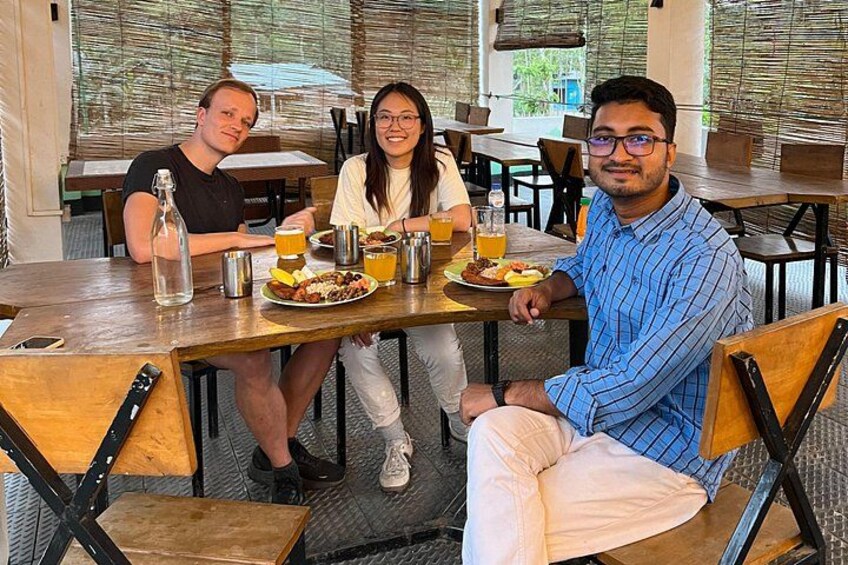 Three people sitting at a wooden table with food and drinks. 2