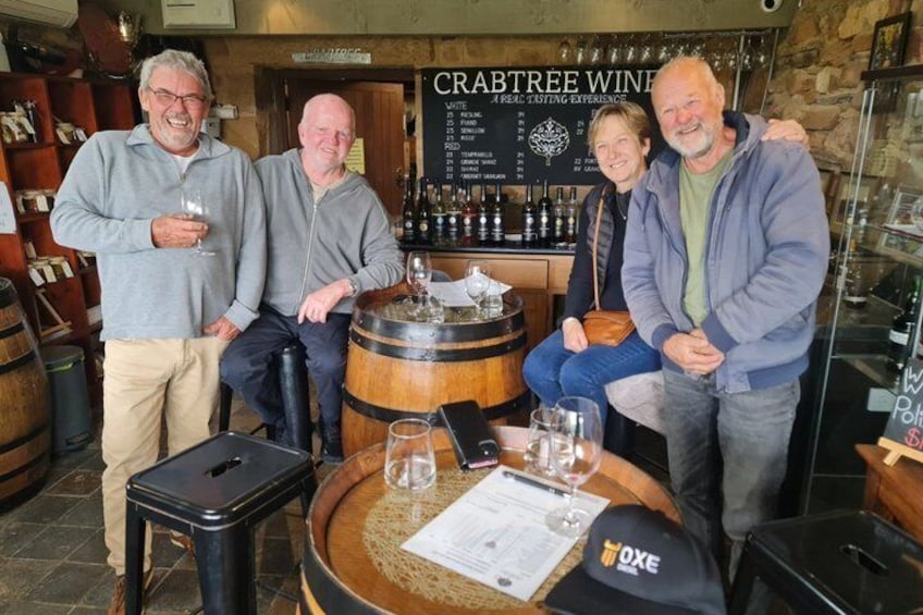 A group of people in a wine tasting room with barrels and a menu board. 1