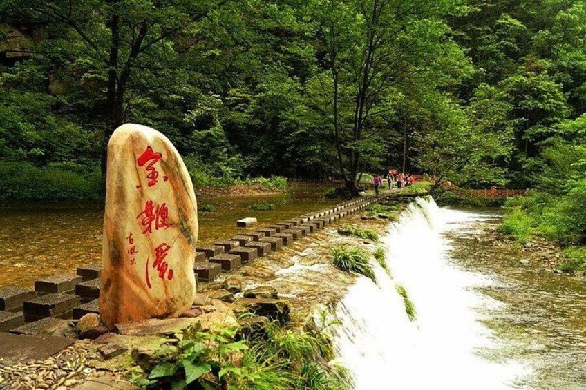 A stone monument with Chinese characters, a stone bridge, and a waterfall in a forested area. 3