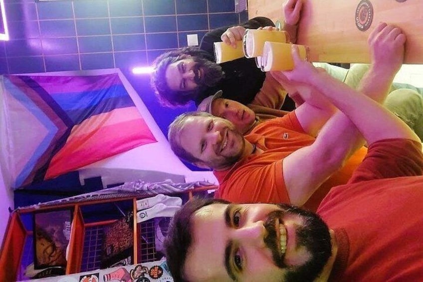 Un groupe de personnes se trouve dans une pièce décorée d’une tapisserie murale aux couleurs vives et d’une structure en bois. 2