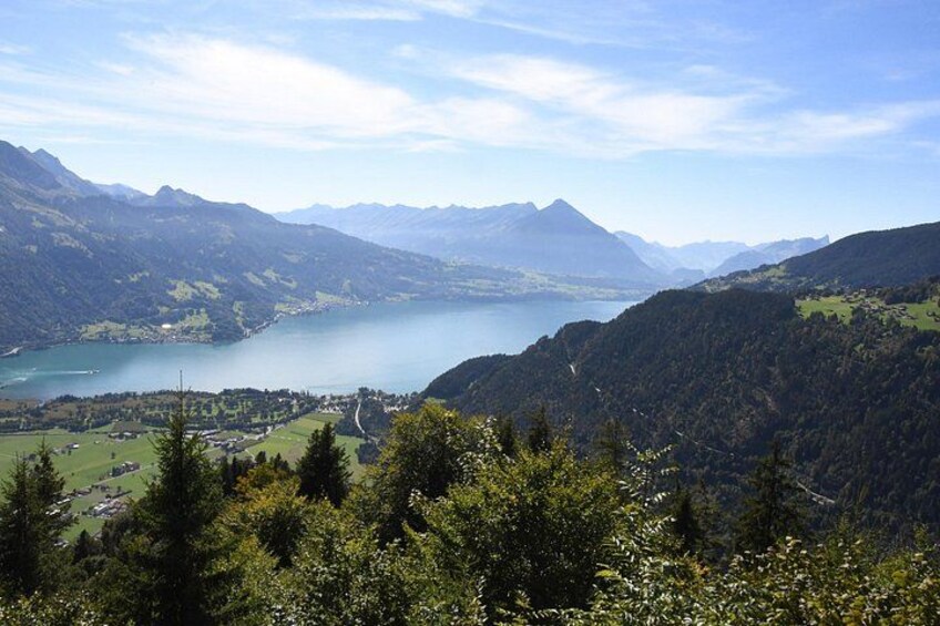 A mountainous landscape with a lake, forested areas, and a small settlement. 5