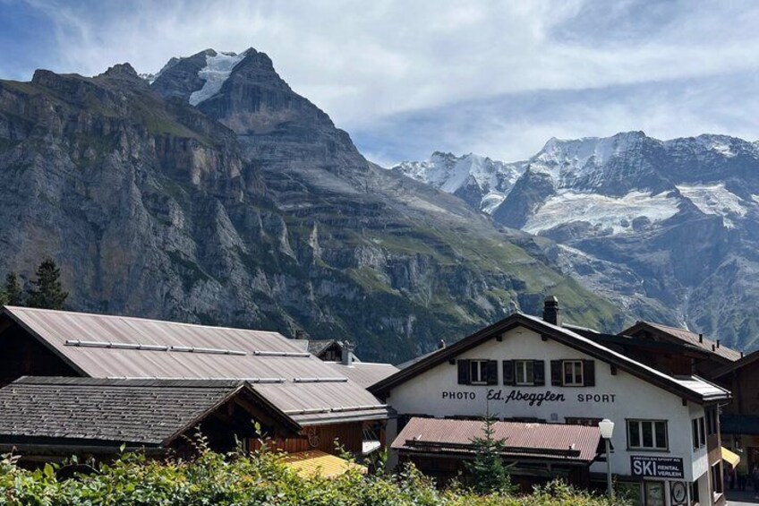 Un village de montagne aux maisons en bois, avec une enseigne indiquant un service de location de matériel de ski, et des sommets enneigés en arrière-plan. 5