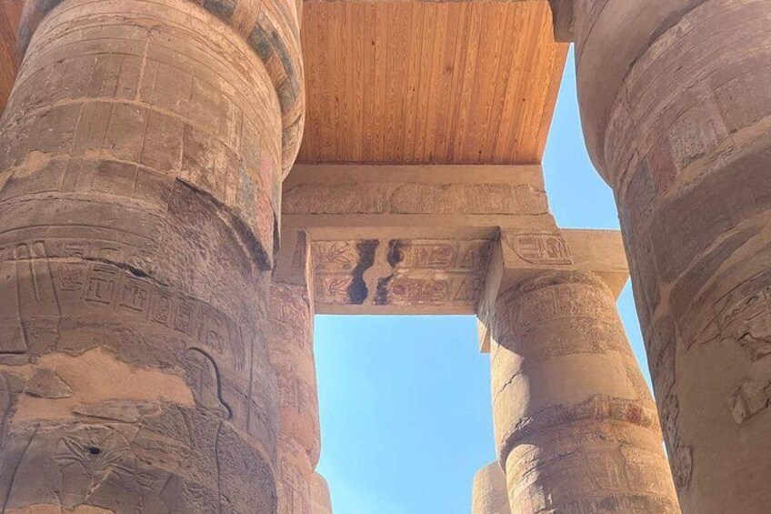 Ancient Egyptian columns with hieroglyphics, a wooden ceiling, and a clear blue sky. 2