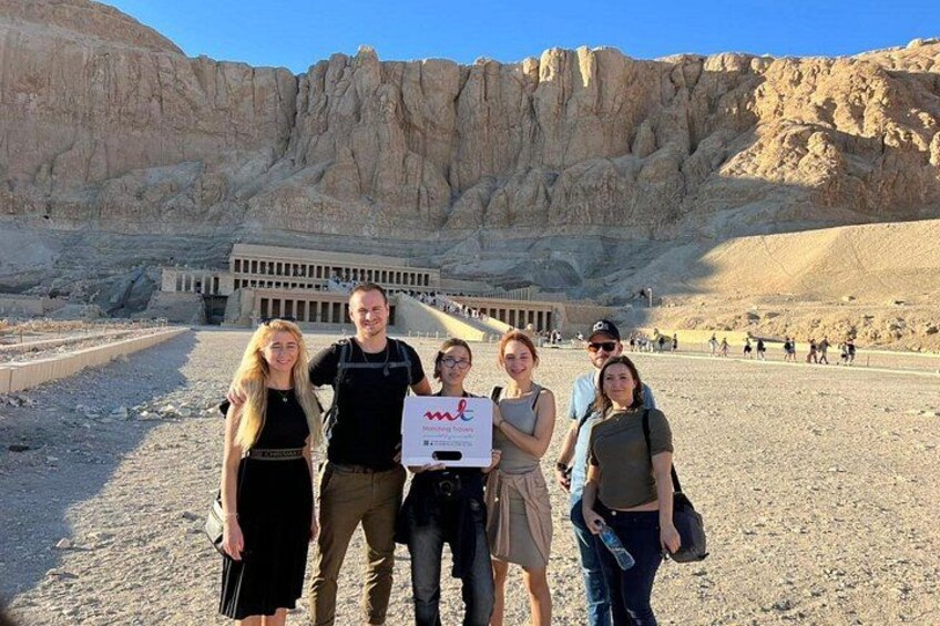 A group of people standing in front of a large, ancient building with a desert landscape in the background. 5