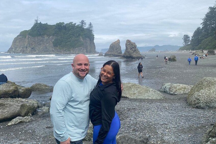 Una pareja está de pie sobre una playa rocosa con olas del océano y formaciones rocosas al fondo. 2