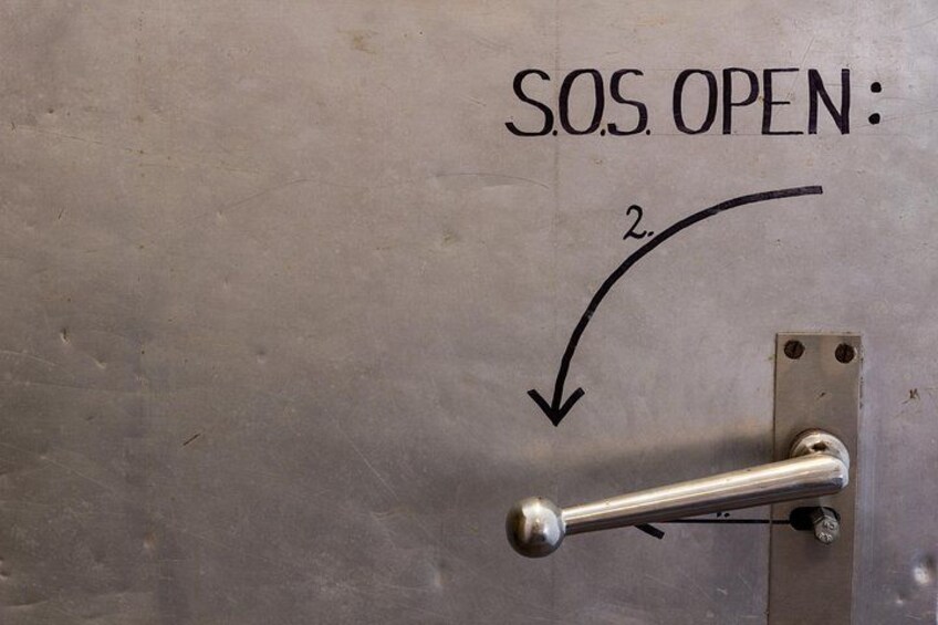 Een metalen deur met een handvat en een label waarop staat: 'S.O.S. OPEN: 2'. 2