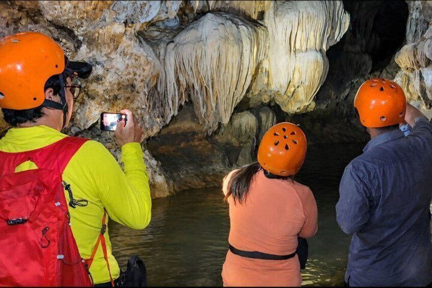 People wearing helmets and taking photos inside a cave with stalactites. 1