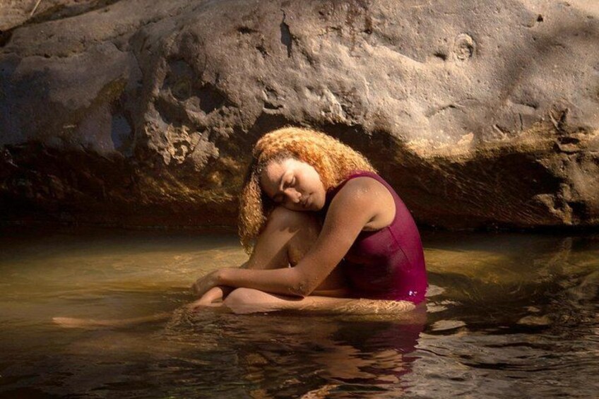 A person sitting in water with a rocky background. 3