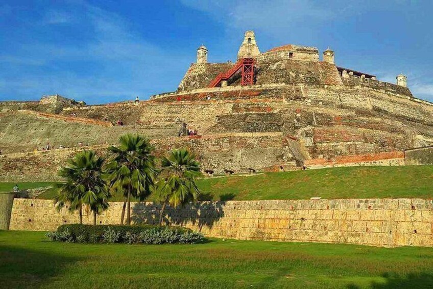 A historic fort with a red drawbridge, palm trees, and a clear sky. 3