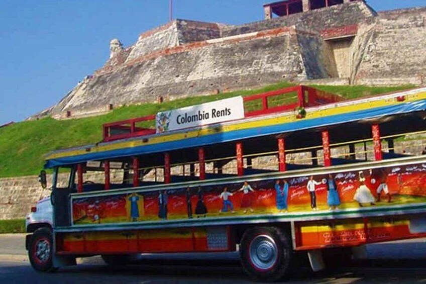 Een kleurrijke bus met een 'Colombia Rents' bord, geparkeerd voor een grote rotsformatie. 2