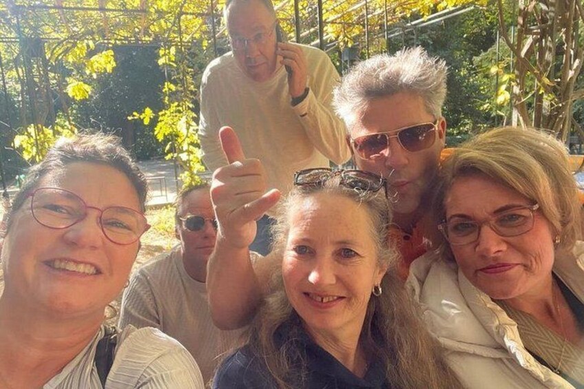 Eine Gruppe von Menschen draußen, mit Bäumen und einem Gebäude im Hintergrund. 2