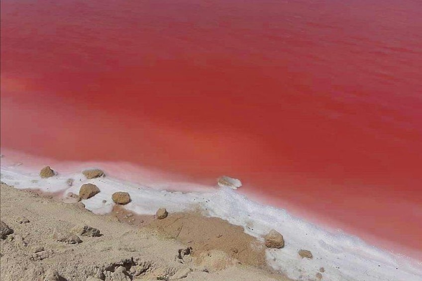 A beach with red water, white sand, and scattered rocks. 4